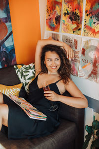 Female painter resting on sofa in studio holding glass of wine