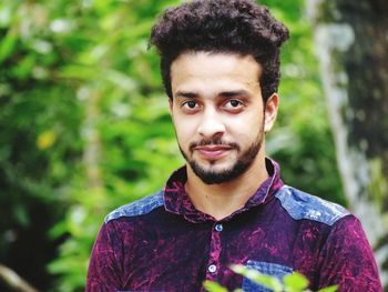 Close-up portrait of young man standing against trees in forest