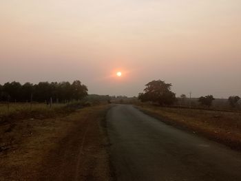 Road amidst field against sky during sunset