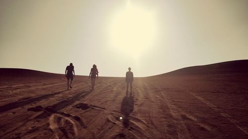 People walking on sand dune in desert against sky