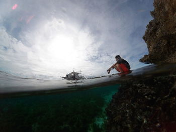 Low angle view of man crouching while sitting in sea against sky