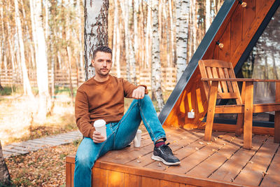 Portrait of young man sitting on wood in forest