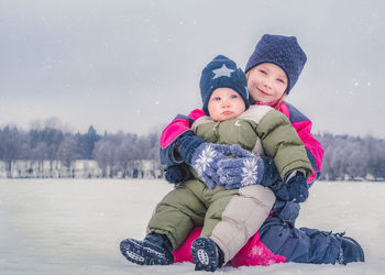 Portrait of siblings sitting on snow covered land