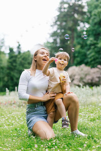 Young caucasian mother and her happy little son are having fun playing with soap bubbles in the park