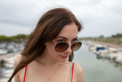 Close-up of thoughtful woman wearing sunglasses while standing against harbor