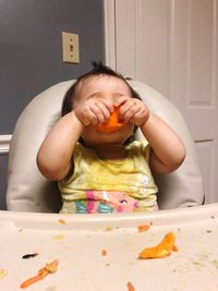 Baby girl eating food while sitting on high chair at home