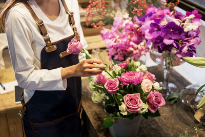 Midsection of florist putting rose in bucket on table
