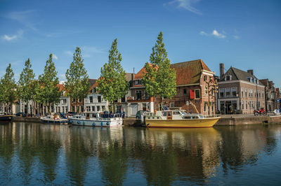 Sailboats moored on canal by buildings against sky