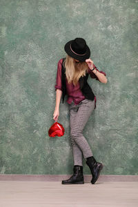 Woman wearing hat while standing against wall