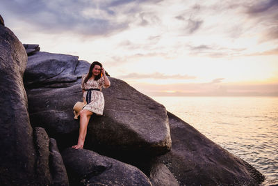Woman standing on rock by sea against sky