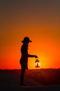 Silhouette woman standing against orange sky