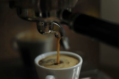 Close-up of machine pouring coffee in cup