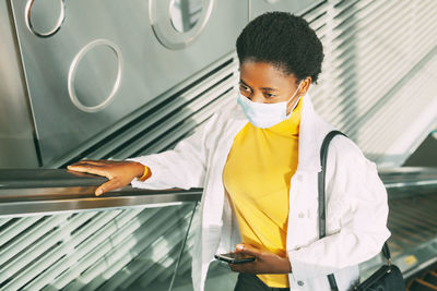 Young woman wearing mask standing on escalator