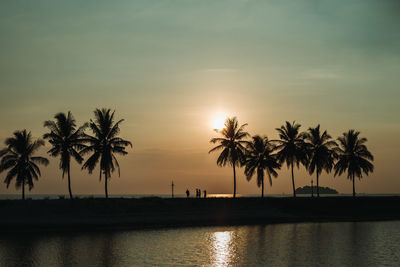 Silhouette palm trees by swimming pool against sky during sunset