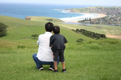 Rear view of couple standing on landscape by sea