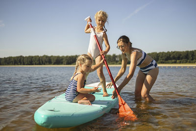Girls with mother on stand up paddle board amidst lake