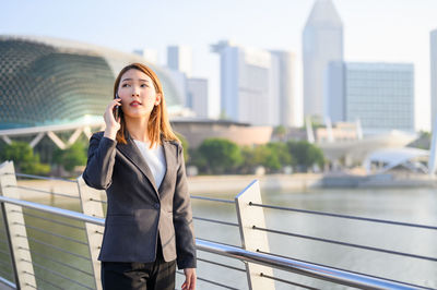 Young woman looking away while standing on railing in city