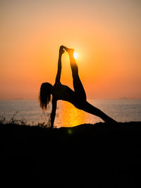 Silhouette woman doing yoga at beach against sky during sunset