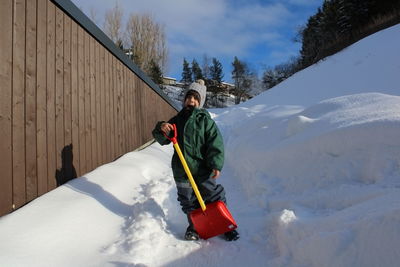 Rear view of boy removing snow on snow covered field