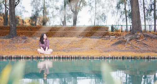 Woman sitting by tree trunk by lake