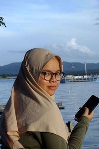 Portrait of young woman using mobile phone against sea