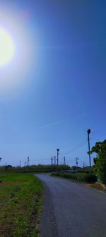 Road amidst field against clear blue sky