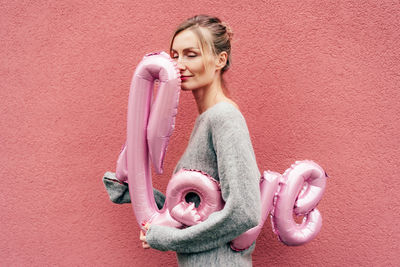 Young woman looking away against pink wall