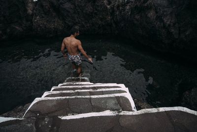 Rear view of shirtless man standing on rock