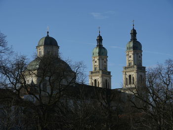 Low angle view of bare trees by st lorenz basilica against blue sky