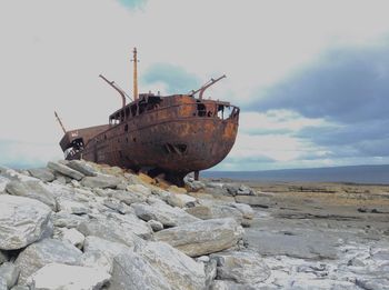 Abandoned boat on beach against sky