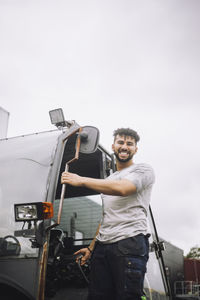 Portrait of happy young construction worker standing at doorway of vehicle