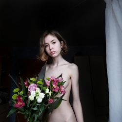 Portrait of naked woman standing by flowers against wall