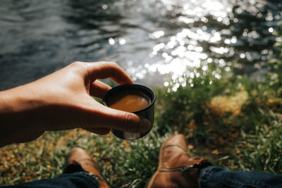 Personal perspective of hand holding thermos mug with coffee