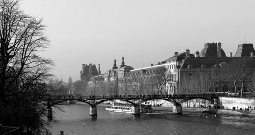 Bridge over river by buildings against clear sky