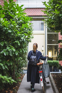 Rear view of female architect with bicycle walking against house