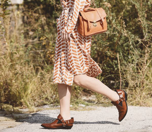 Low section of woman walking on footpath during sunny day