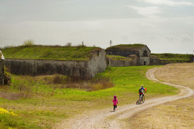 People walking on road amidst field against sky