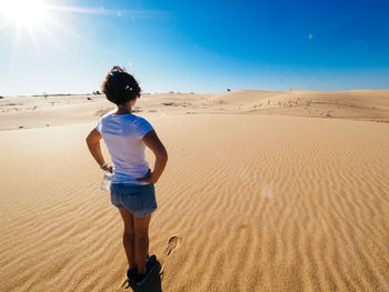 Rear view of boy on sand at beach against clear sky