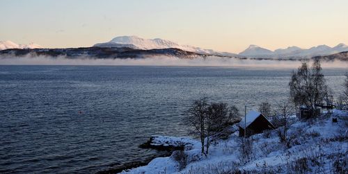 Scenic view of lake by snowcapped mountains against sky during sunset