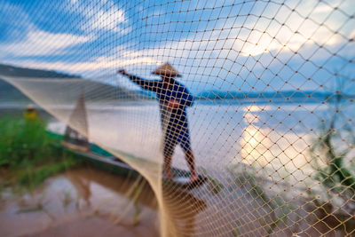 In the early morning before sunrise, an asian fisherman on a wooden boat casts a net for catching 