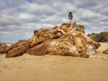 Rear view of woman standing on rock at beach against sky