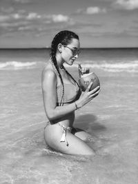 Side view of woman wearing bikini while drinking coconut water in sea