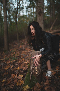 Portrait of woman by tree stump in forest