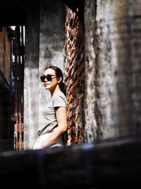 Side view of woman wearing sunglasses standing against wall