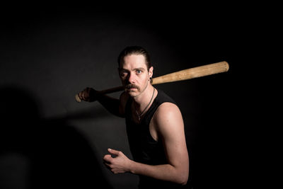 Portrait of angry man with baseball bat standing against black background