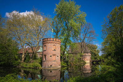 Old abandoned building by trees against blue sky