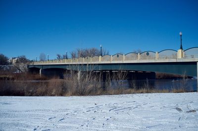 Bridge over frozen river against clear blue sky