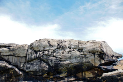 Low angle view of rock formations against cloudy sky during sunny day