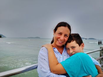 Portrait of son embracing mother against sea
