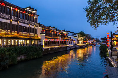 Illuminated buildings by river against sky at night